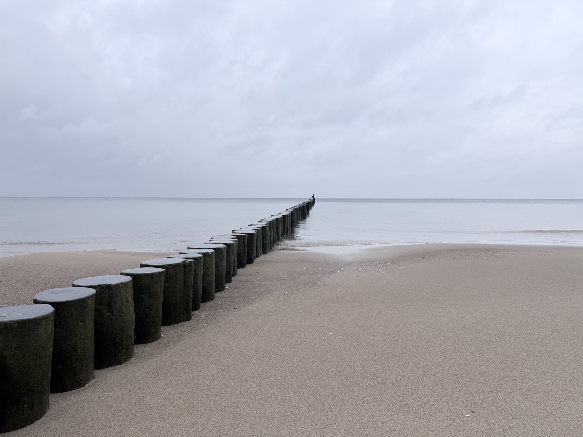 Bewölkter Tag an der polnischen Ostsee am Strand, von der Ecke links unten in die Mitte führt ein Holzwall.