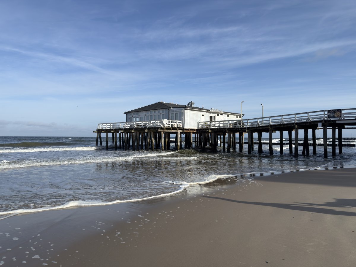 Ein weißes Pier mir Haus auf Holzstelzen am Strand.
